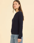 Woman wearing a navy sweater and light blue jeans on a beige background