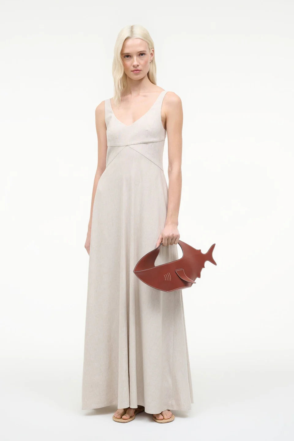 Woman in a long beige dress holding a fish-shaped bag on a white background
