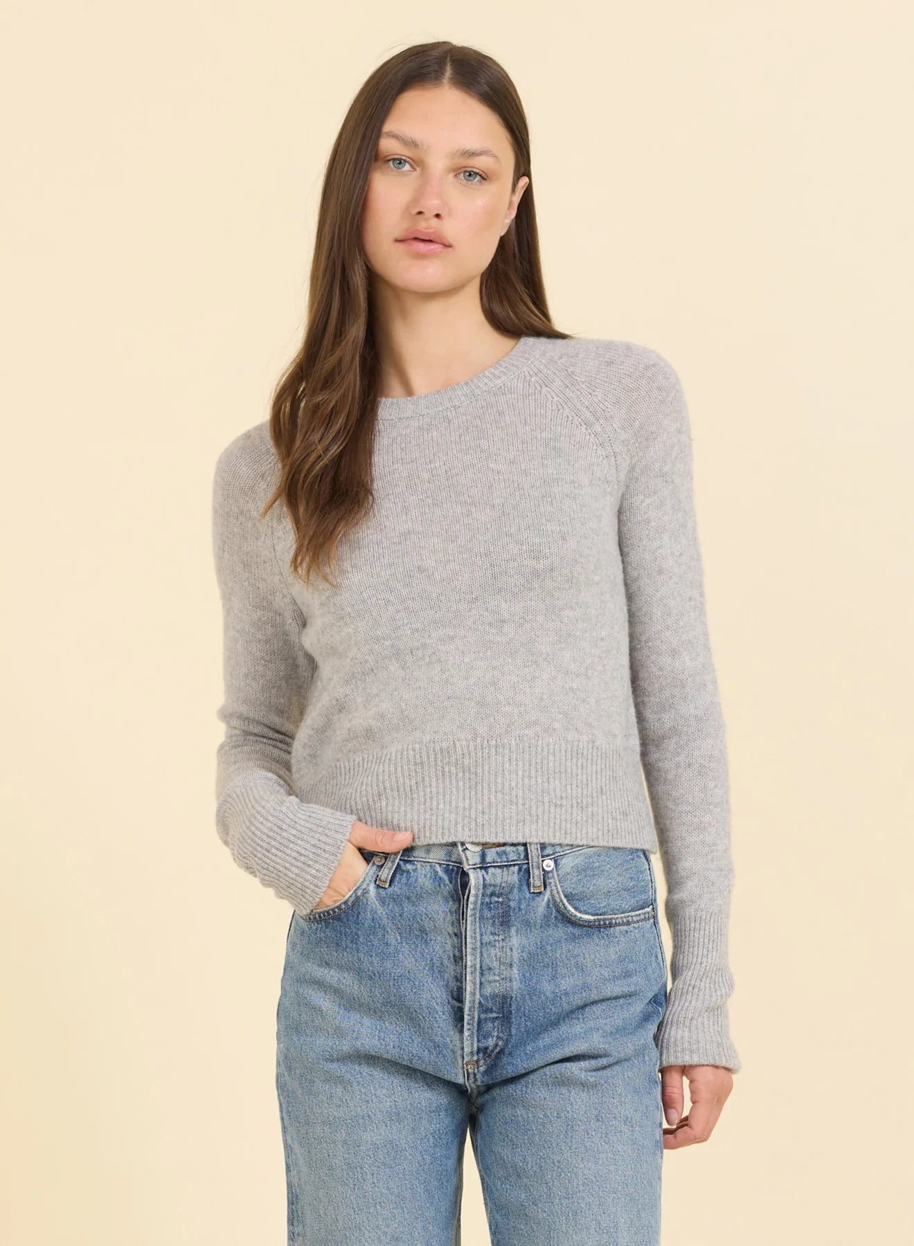 Woman wearing a gray sweater and blue jeans on a beige background
