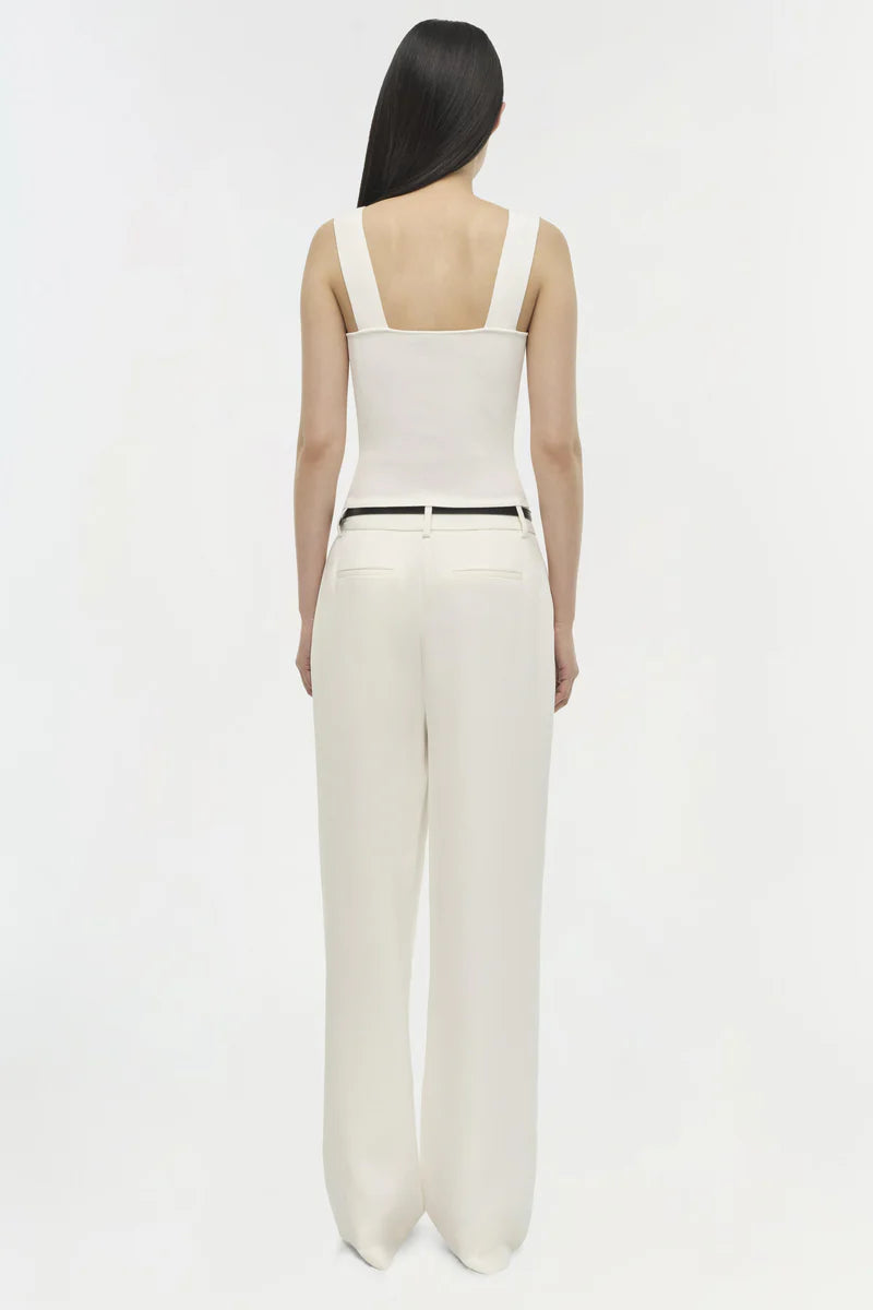 Woman wearing a white sleeveless top and pants on a white background back view