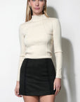 woman wearing a cream long sleeve top with a black mini skirt on a white background
