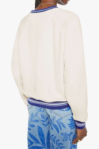 Person wearing a cream sweater with blue trim and blue floral pants on a white background