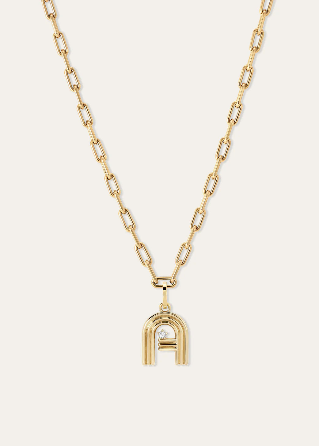 A gold chain necklace featuring a stylized lowercase 'a' pendant with a diamond accent, displayed against a light off-white background.