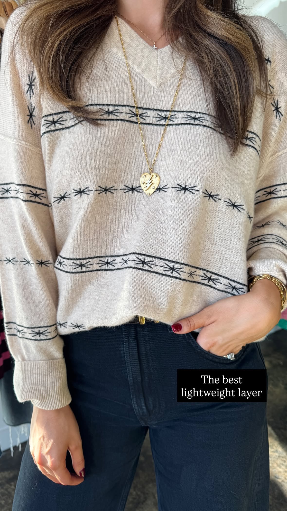 Person wearing a beige sweater with black patterns and dark jeans