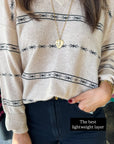 Person wearing a beige sweater with black patterns and dark jeans