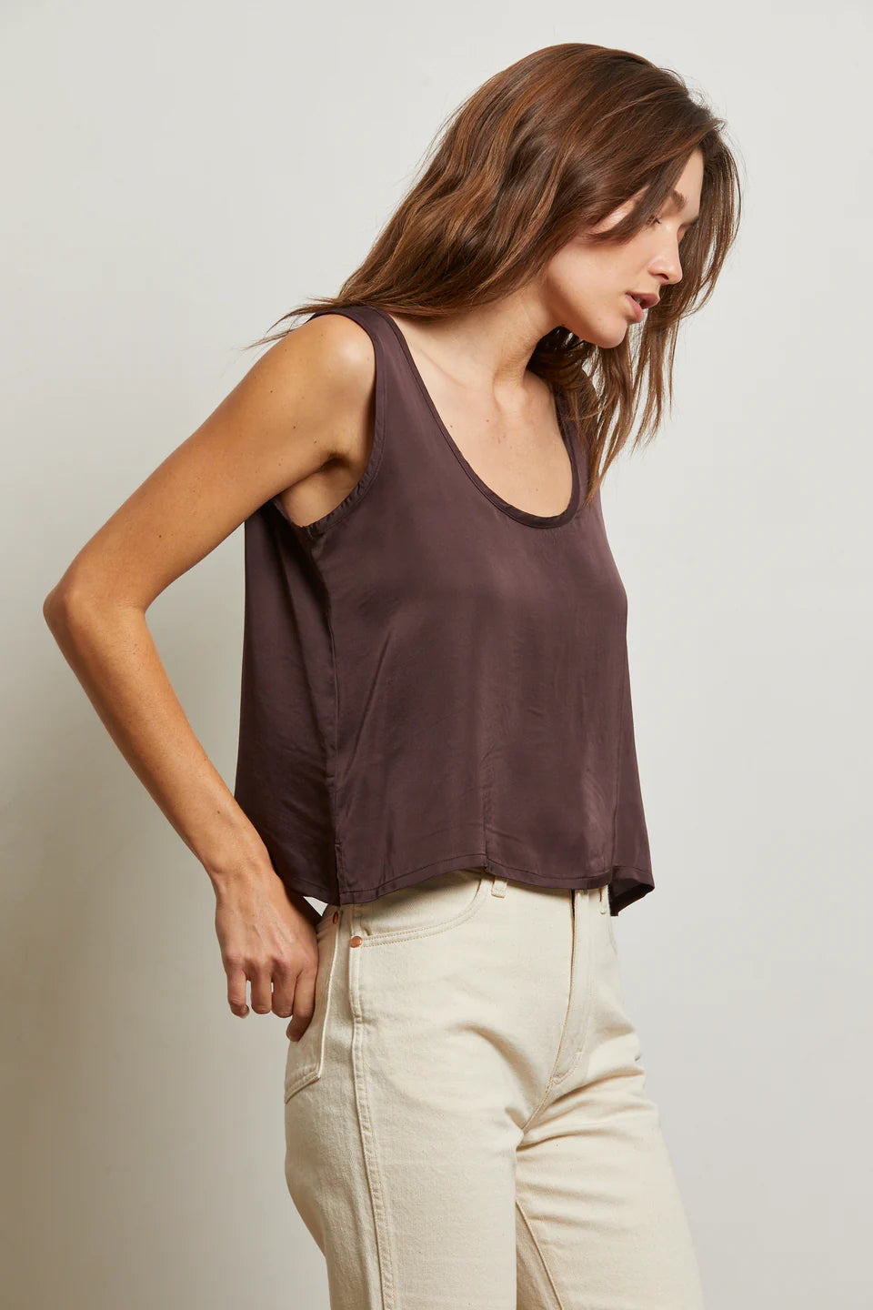Woman wearing a brown tank top and beige pants against a plain background side view