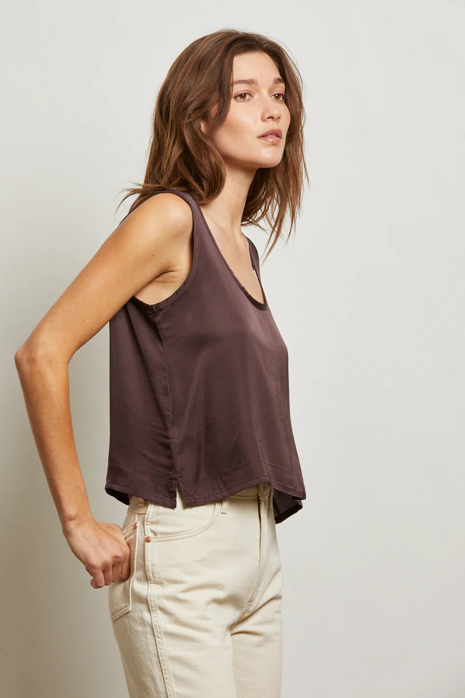 Woman wearing a sleeveless brown top and beige pants against a plain background side view