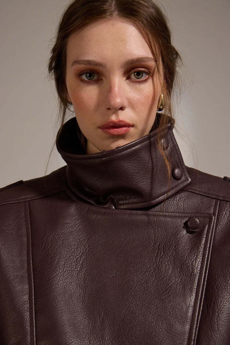 Close-up of a person wearing a brown leather coat against a neutral background