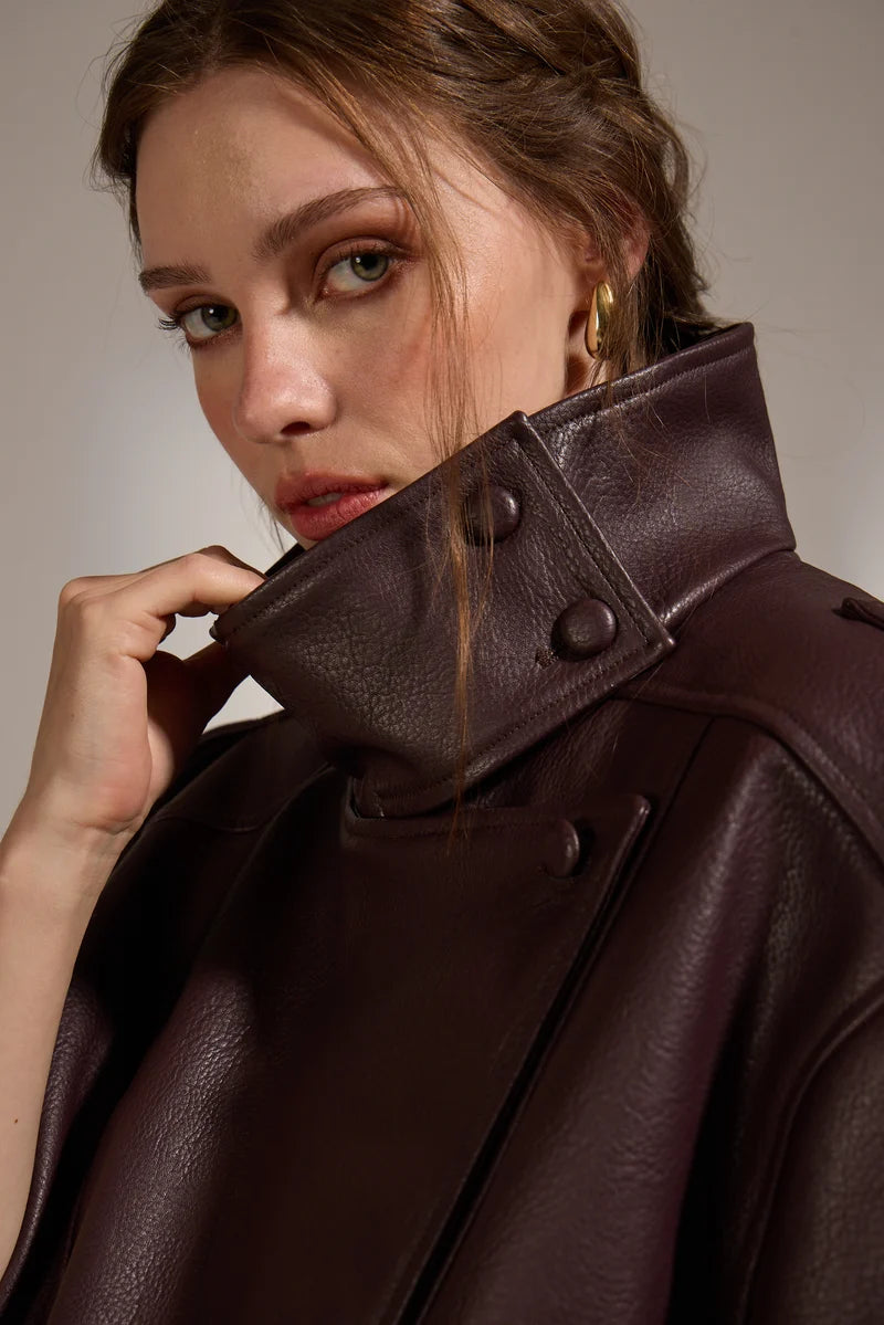 Woman wearing a brown leather coat with a neutral background