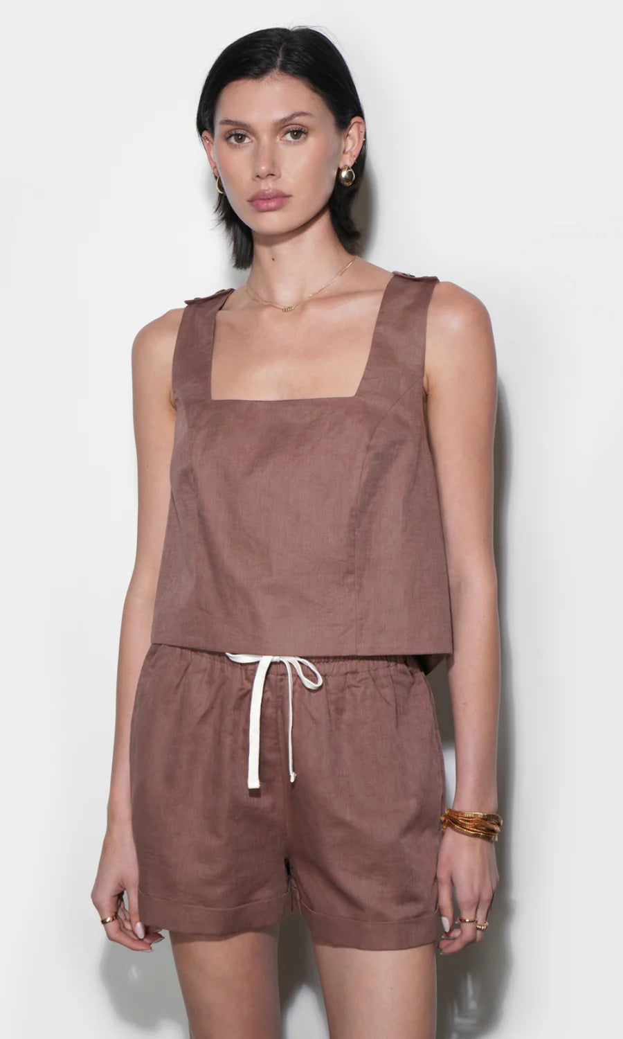 Woman wearing a brown sleeveless top and shorts against a white background