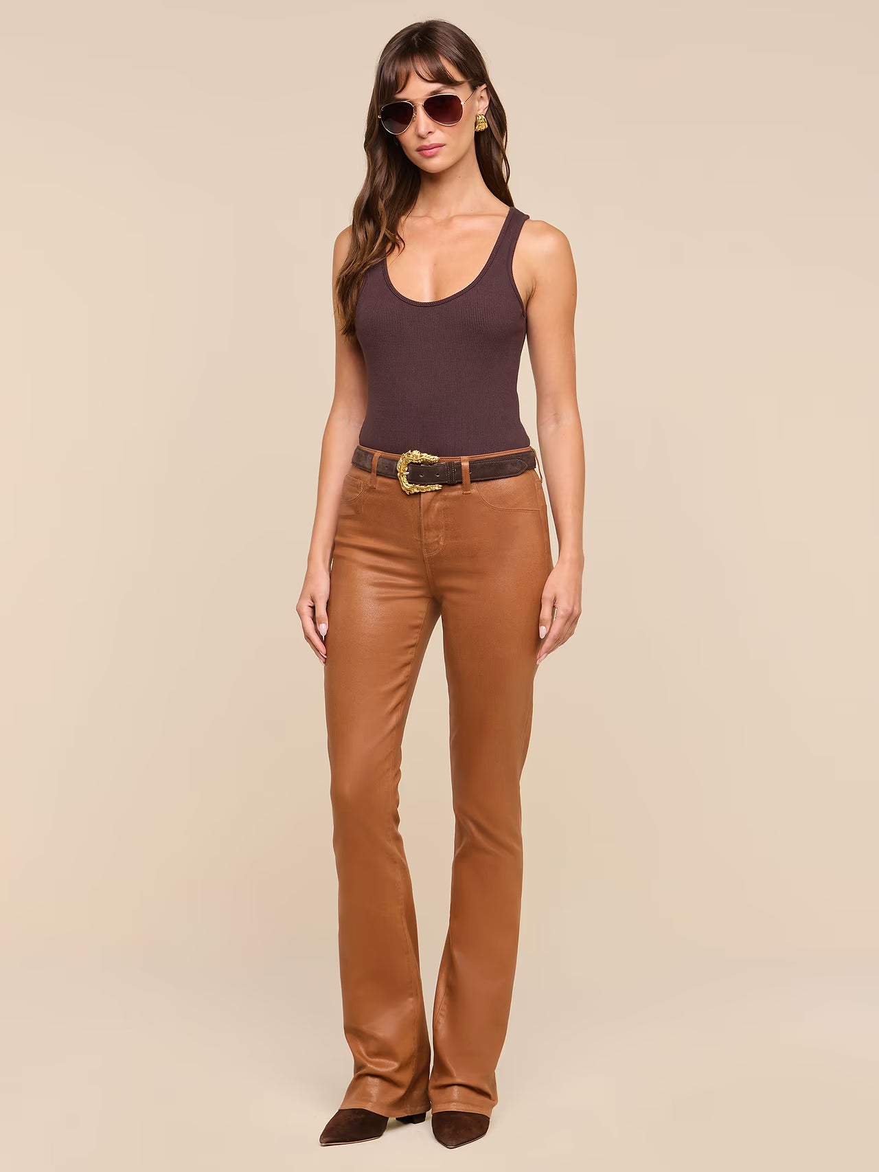 A woman modeling a dark brown ribbed tank top and Selma Coated Bootcut Jean Java Coated with a black belt, photographed against a solid beige studio background.