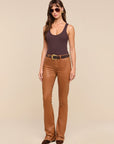 A woman modeling a dark brown ribbed tank top and Selma Coated Bootcut Jean Java Coated with a black belt, photographed against a solid beige studio background.