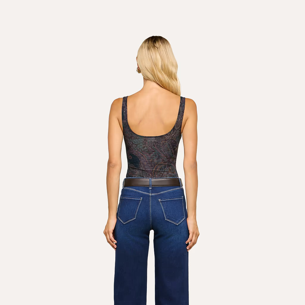 A woman viewed from the back wearing a dark patterned scoop-neck tank top and blue jeans against a plain light background.