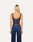 A woman viewed from the back wearing a dark patterned scoop-neck tank top and blue jeans against a plain light background.