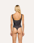 A woman viewed from the back wearing a one-piece swimsuit with a dark navy and black paisley pattern, set against a solid off-white background.