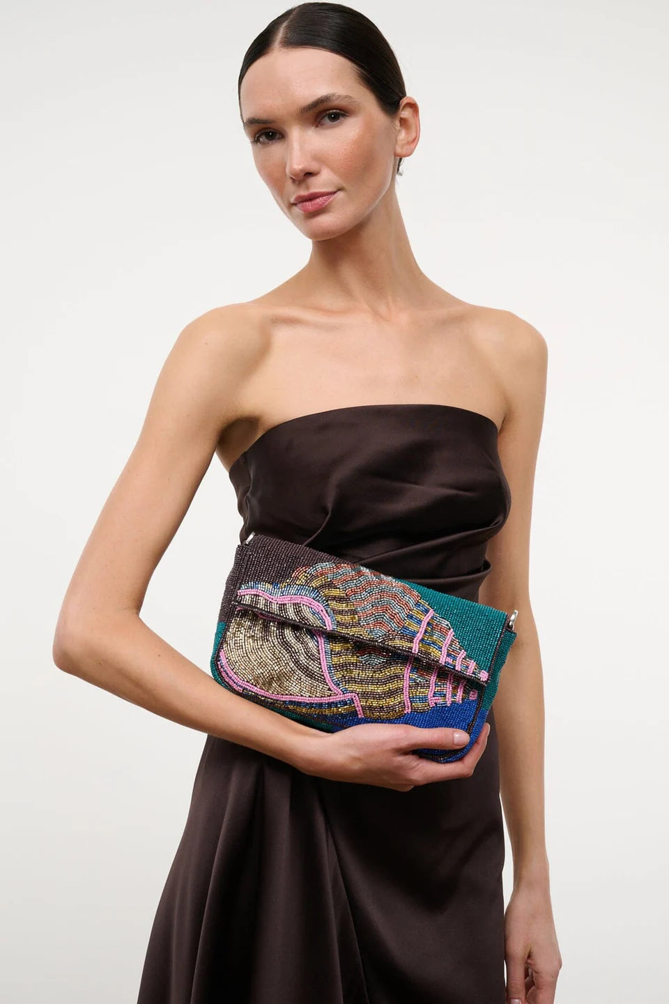 Woman holding a colorful beaded clutch against a plain background