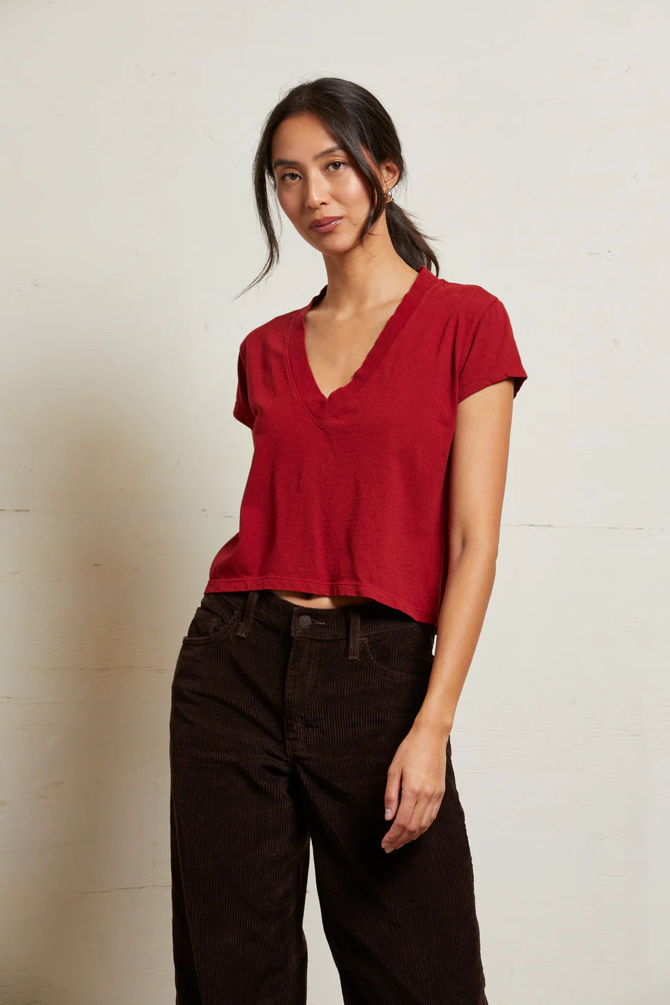 Woman wearing a red top and dark pants against a plain background front view
