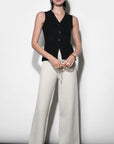 Woman wearing a black sleeveless top and white pants against a white background
