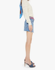 Woman wearing a colorful headscarf, white sweater, and denim shorts on a white background