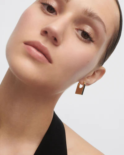 Close-up of a person wearing a gold earring on a plain background
