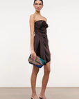 Woman wearing a strapless brown dress holding a colorful beaded clutch against a white background