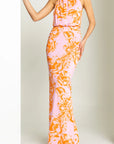 Woman wearing a pink and orange floral dress against a plain background