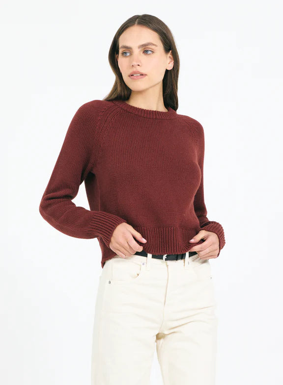 Woman wearing a maroon sweater and white pants on a white background