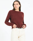 Woman wearing a maroon sweater and white pants on a white background