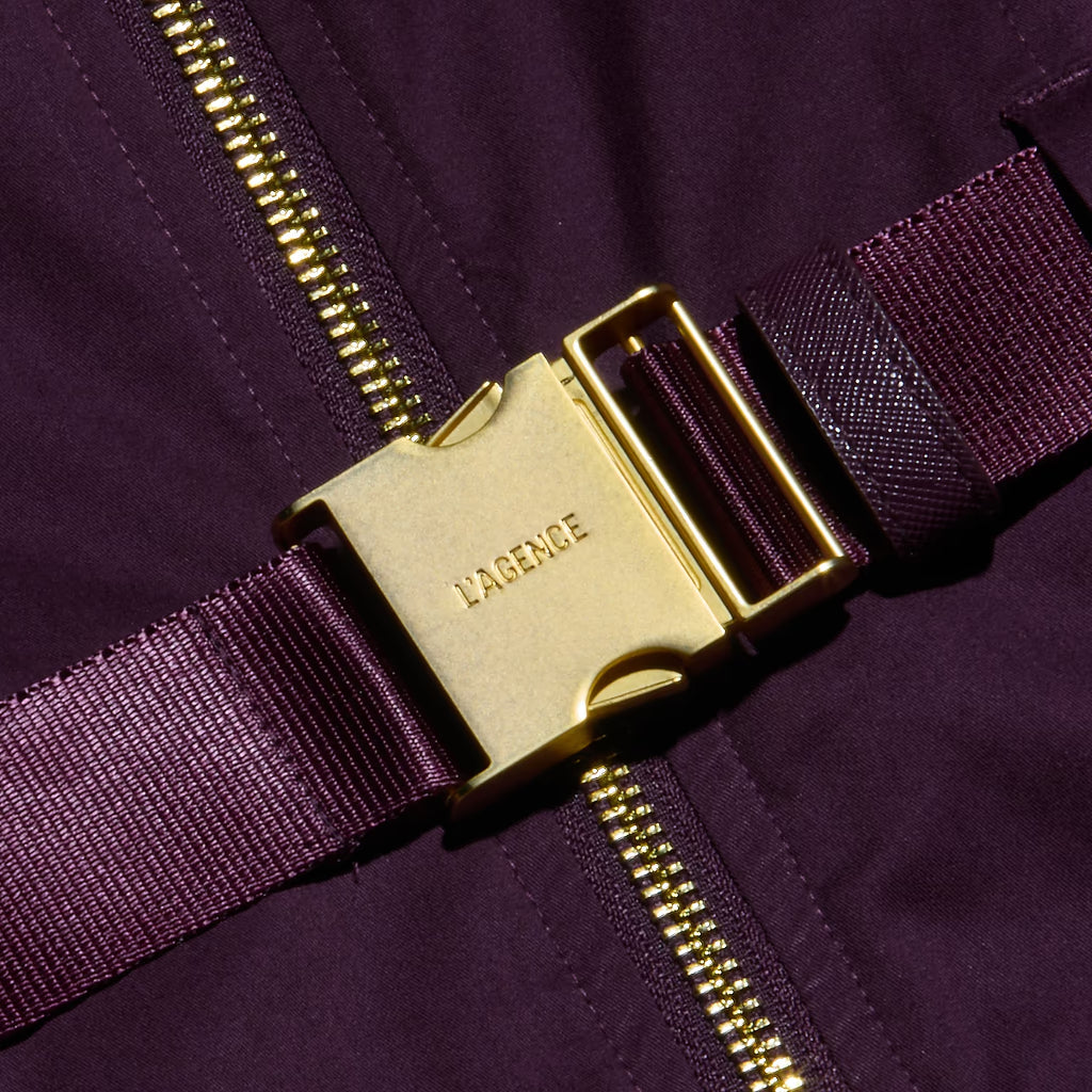 Close-up of a dark purple garment with a wide matching purple woven strap and a prominent gold-tone metal buckle engraved with the brand name LABERGE.