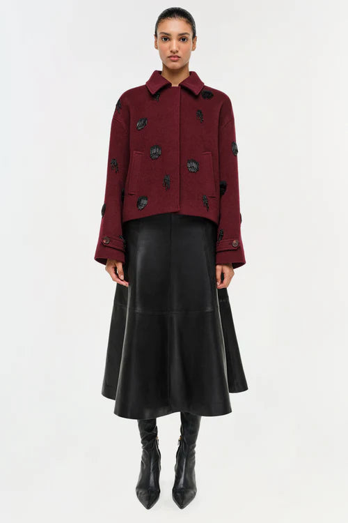Woman wearing a burgundy jacket with black buttons and a black leather skirt on a white background