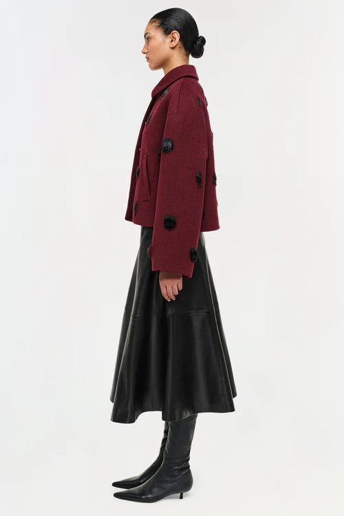 Person wearing a burgundy coat with black buttons on a white background