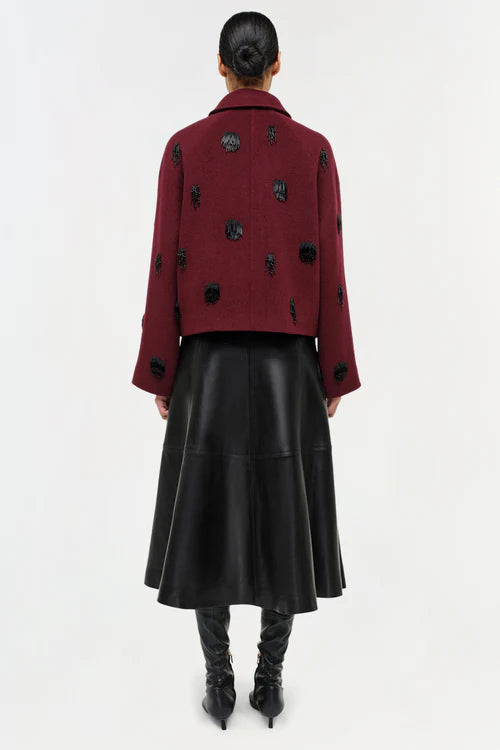 Person wearing a burgundy coat with black polka dots and a black leather skirt on a white background