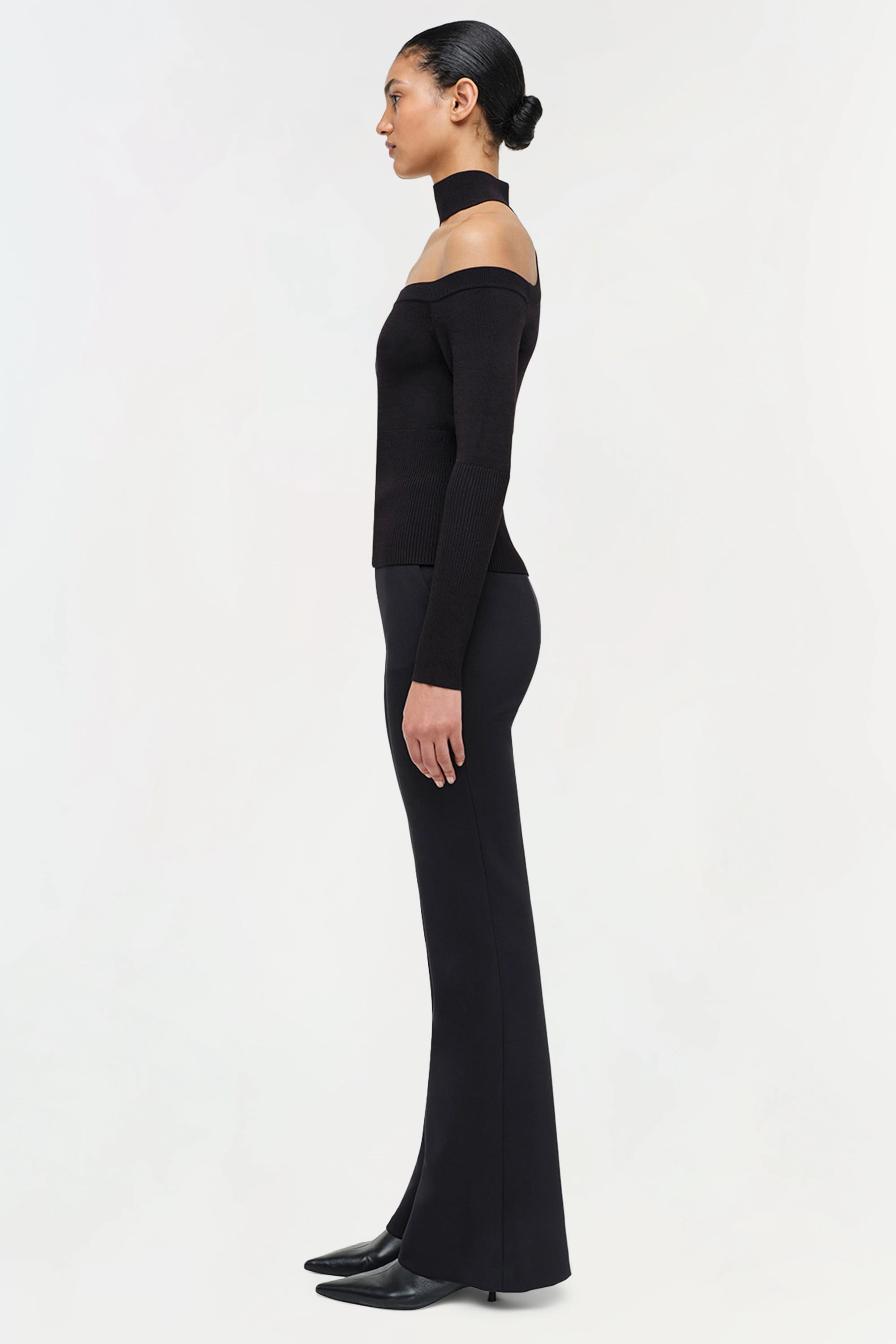 Woman wearing a black off-shoulder dress with long sleeves on a white background side
