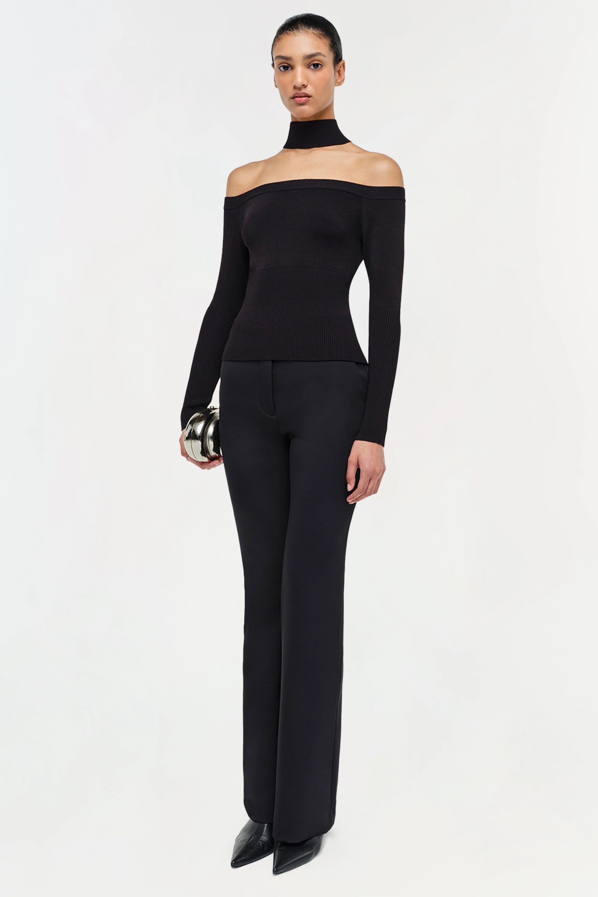 Woman wearing a black off-shoulder top and black pants on a white background