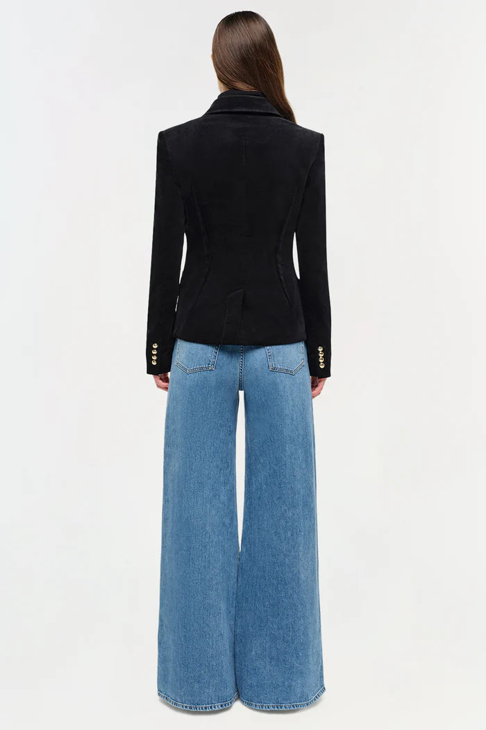 Person wearing a black blazer and blue jeans on a white background