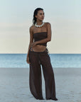 model wearing brown one piece bathing suit with brown mesh coverup pants on the beach