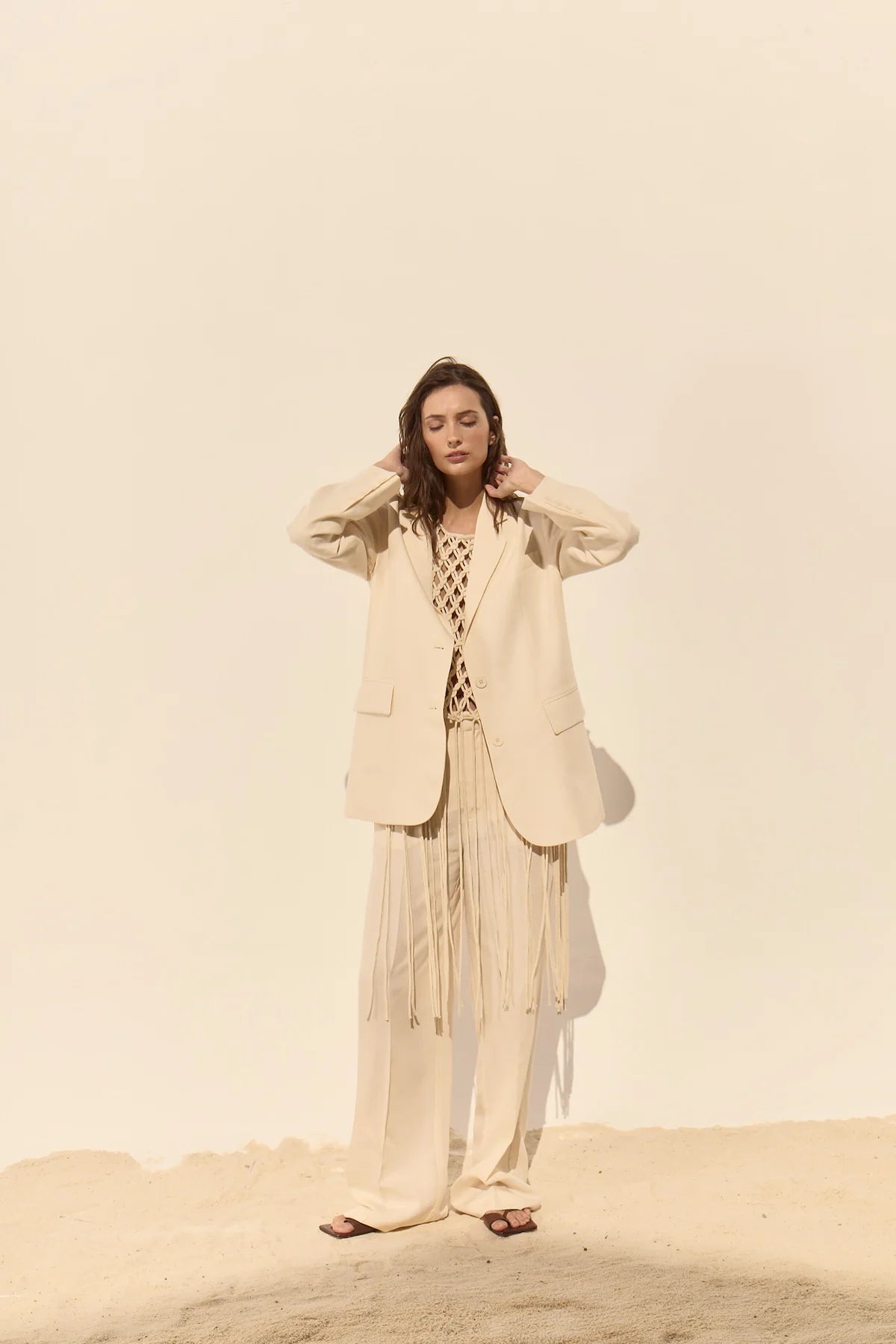 Woman in a beige suit standing on a sandy surface with a plain background