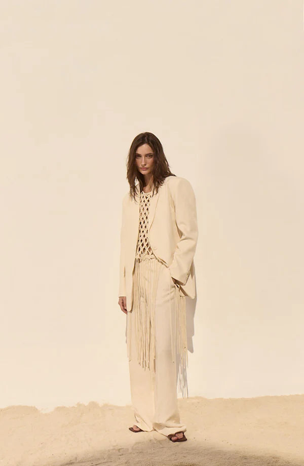 Woman wearing a beige outfit with fringe details against a plain background