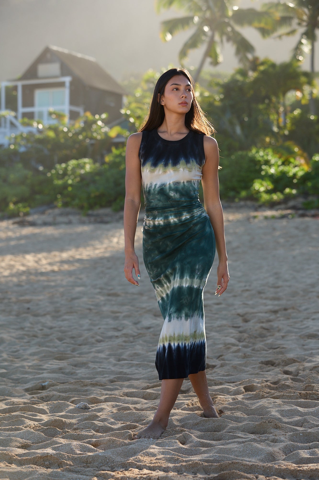 Woman wearing a tie-dye dress on a beach with palm trees in the background