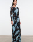 A woman modeling a long-sleeve maxi dress with a blue, brown, and black abstract tie-dye pattern, standing against a plain white studio background.