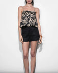 Woman wearing a black and gold patterned top with black shorts on a white background