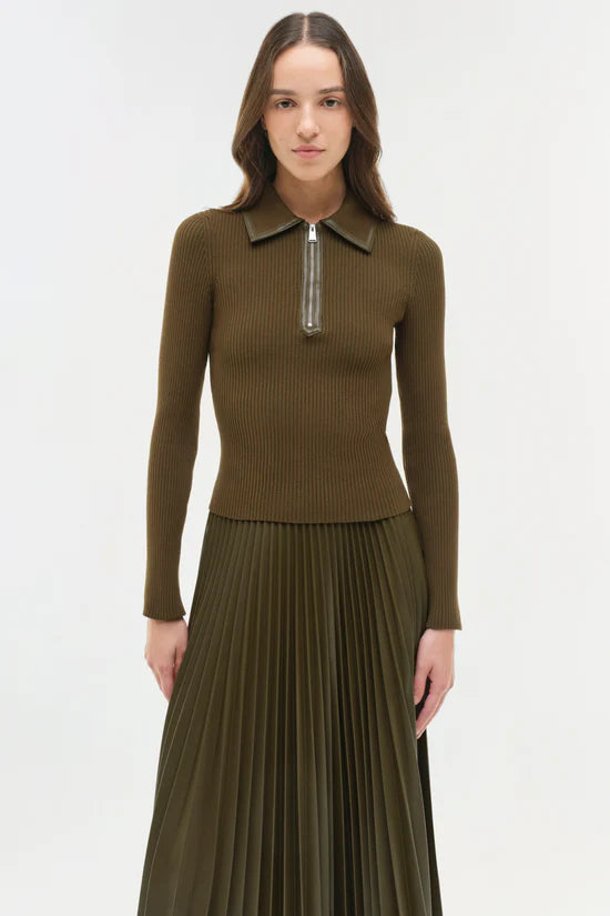 Woman wearing a brown/green ribbed sweater with a zipper and pleated skirt on a white background