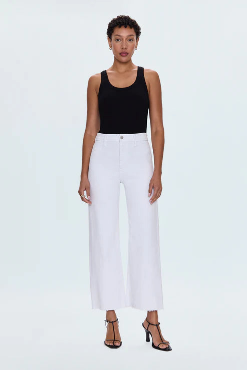 Woman wearing a black tank top and white pants on a light gray background