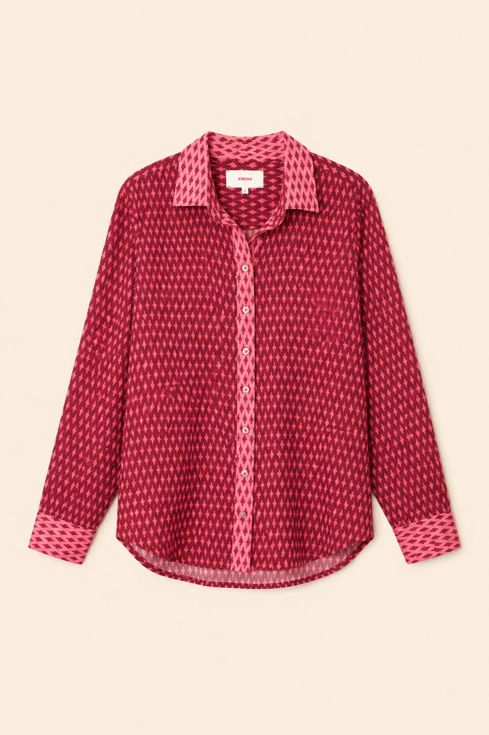 A long-sleeve button-up shirt with a dense small-scale geometric pattern in shades of red and pink, featuring a solid pink patterned collar and cuffs, laid flat against a light beige background.