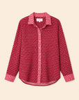 A long-sleeve button-up shirt with a dense small-scale geometric pattern in shades of red and pink, featuring a solid pink patterned collar and cuffs, laid flat against a light beige background.