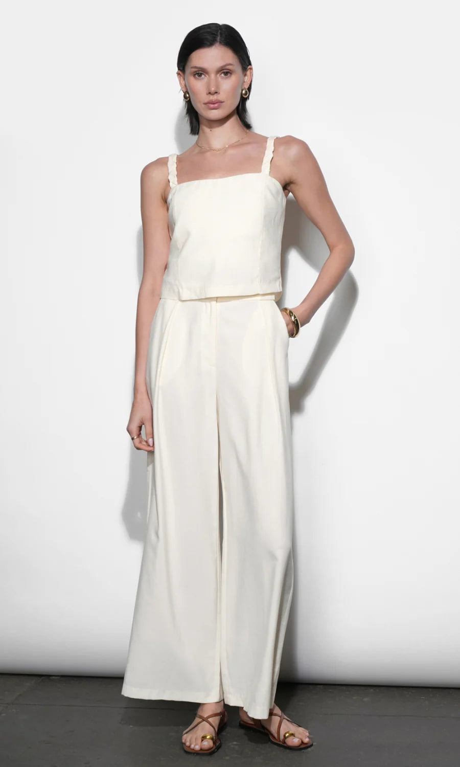 Woman wearing a white sleeveless top and wide-leg pants against a plain background