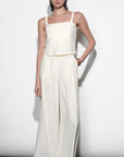Woman wearing a white sleeveless top and wide-leg pants against a plain background