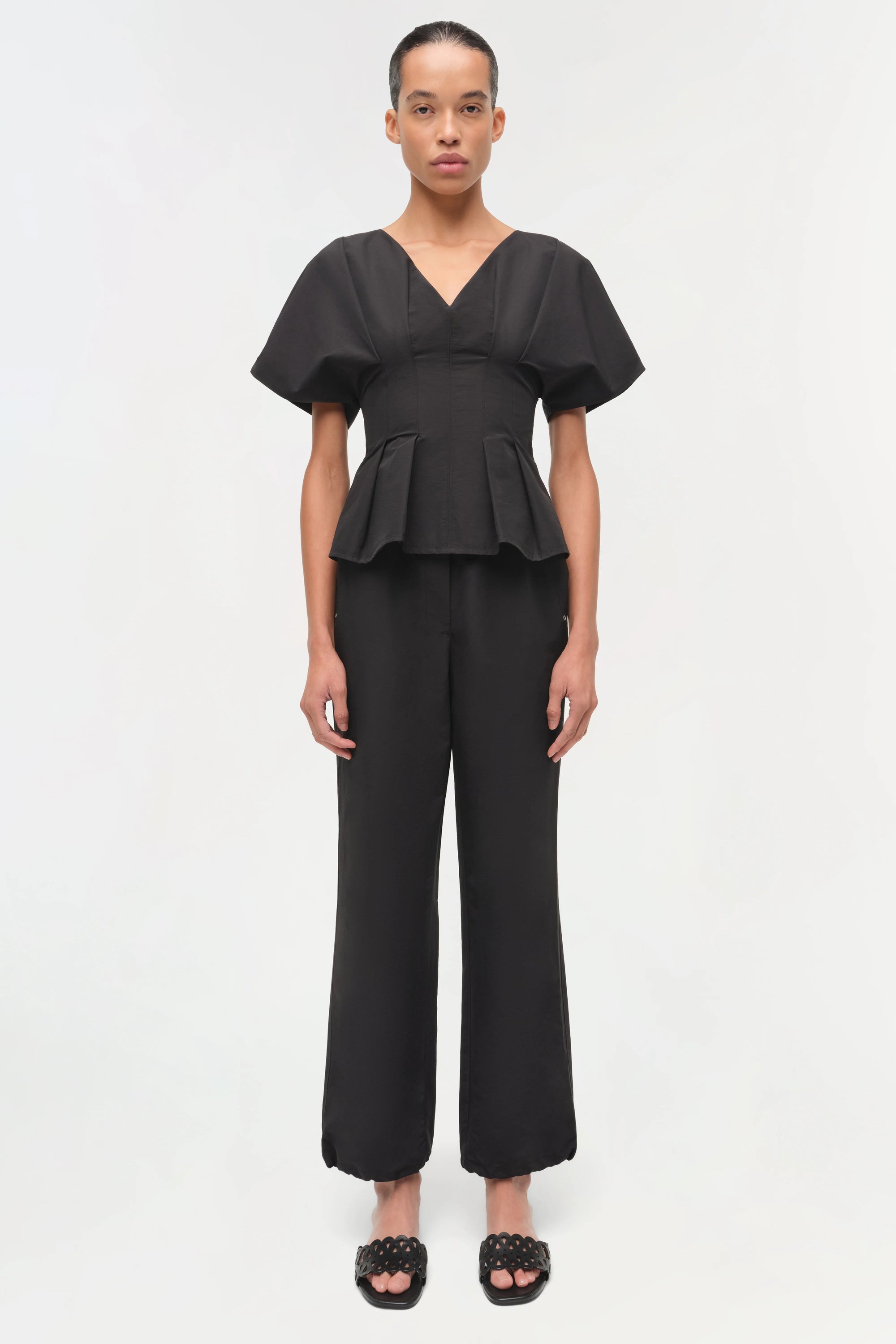Woman wearing a black peplum top and wide-leg pants on a white background