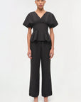 Woman wearing a black peplum top and wide-leg pants on a white background