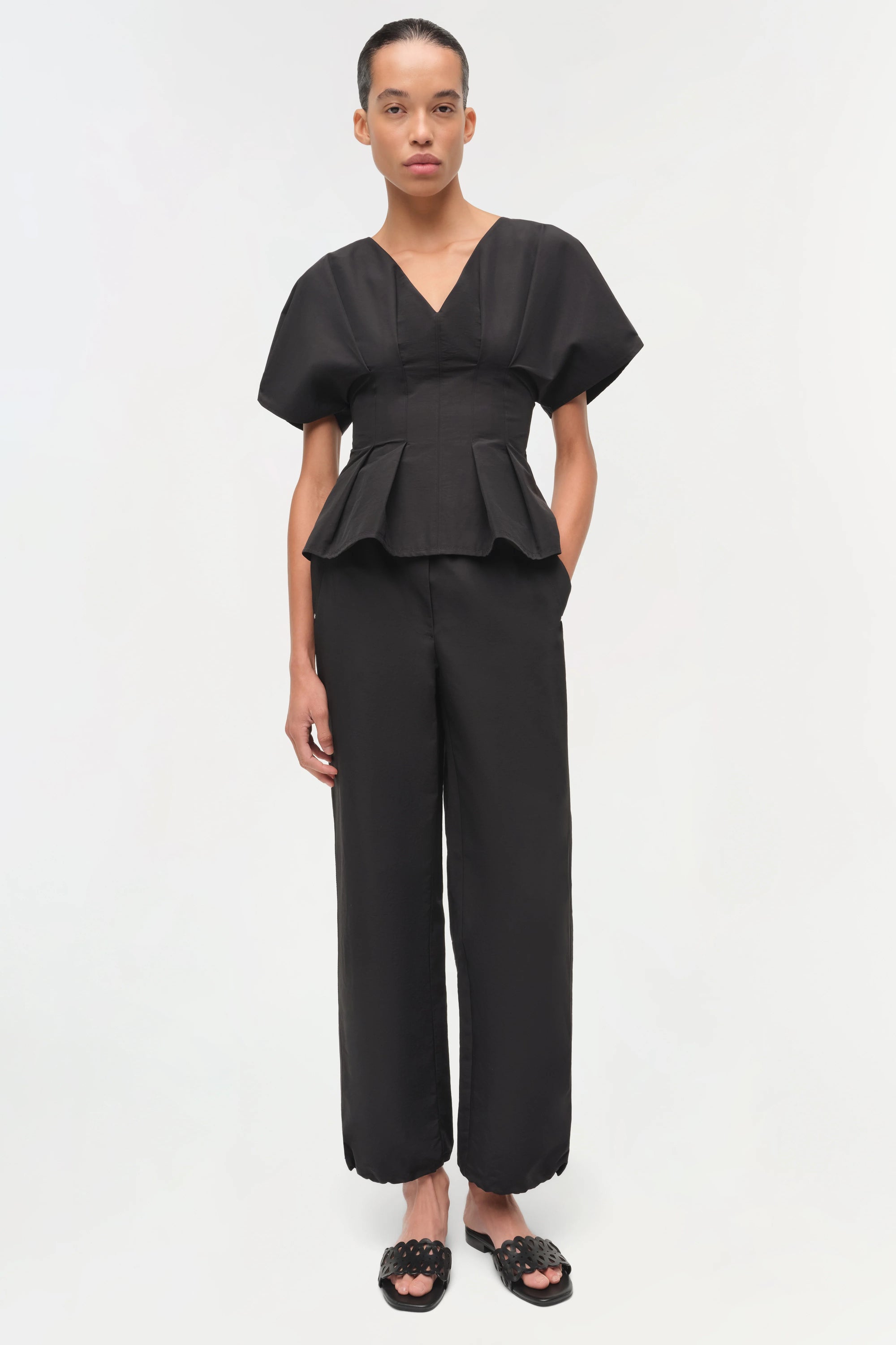 Woman wearing a black peplum top and wide-leg pants on a white background